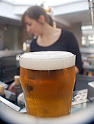 Ett glas öl på en bardisk med bartendern i bakgrunden