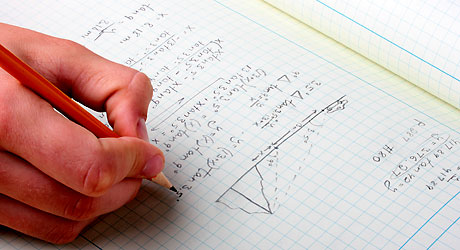 En hand skriver matematiska formler i en anteckningsbok