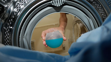 En tvätt maskin sedd innifrån. En hand sticks in med en boll med tvättmedel.