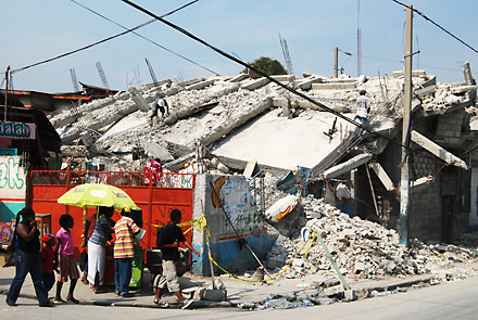 Ett hus som rasat samman efter jordbävningen. Bredvid ruinen fortgår livet.