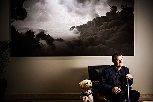 Magnus Berglund sitter i en fåtölj med en stor tavla med moln på bakom sig.